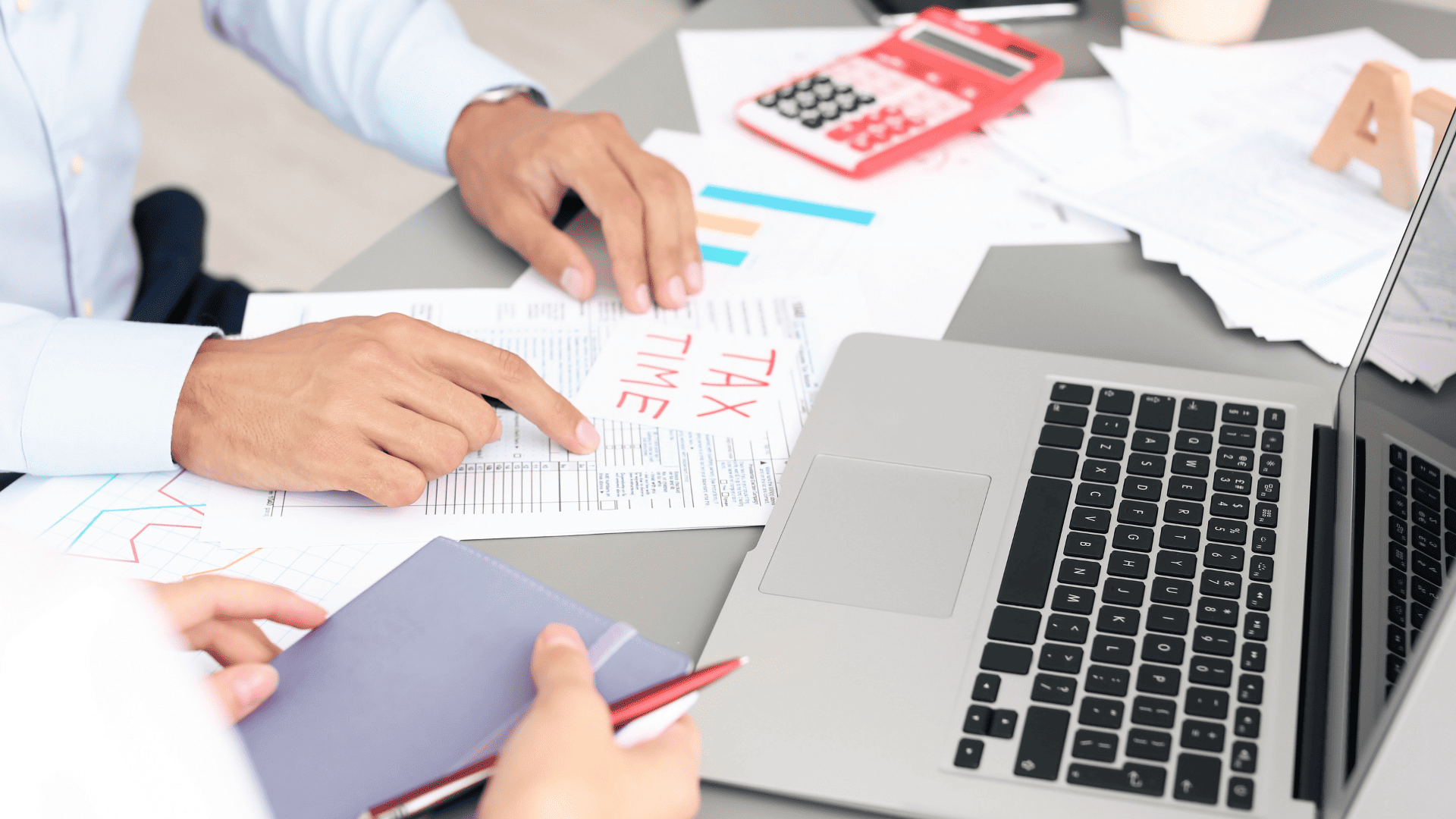 Two men sitting at a desk with a laptop and pieces of paper